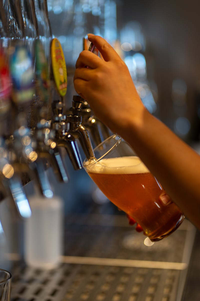 A person is holding a glass of beer in front of a tap